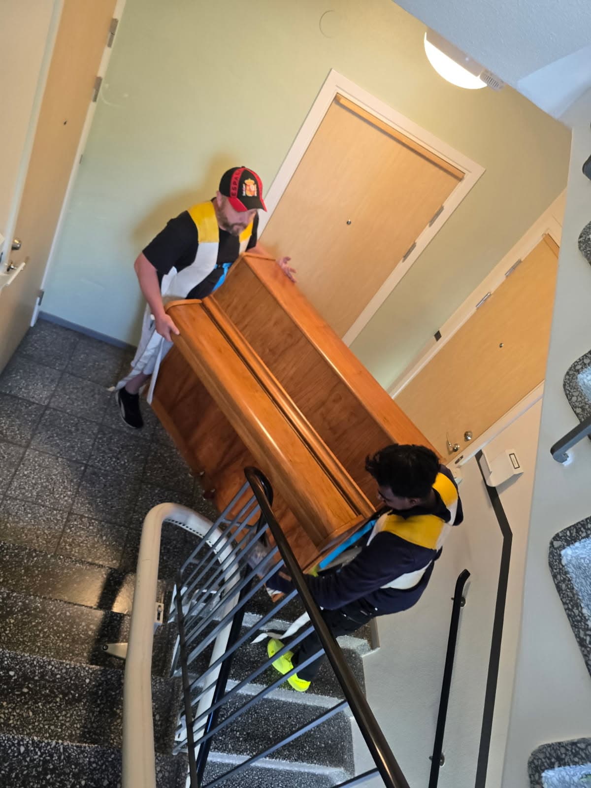 Två personer bär en möbel nerför ett trapphus